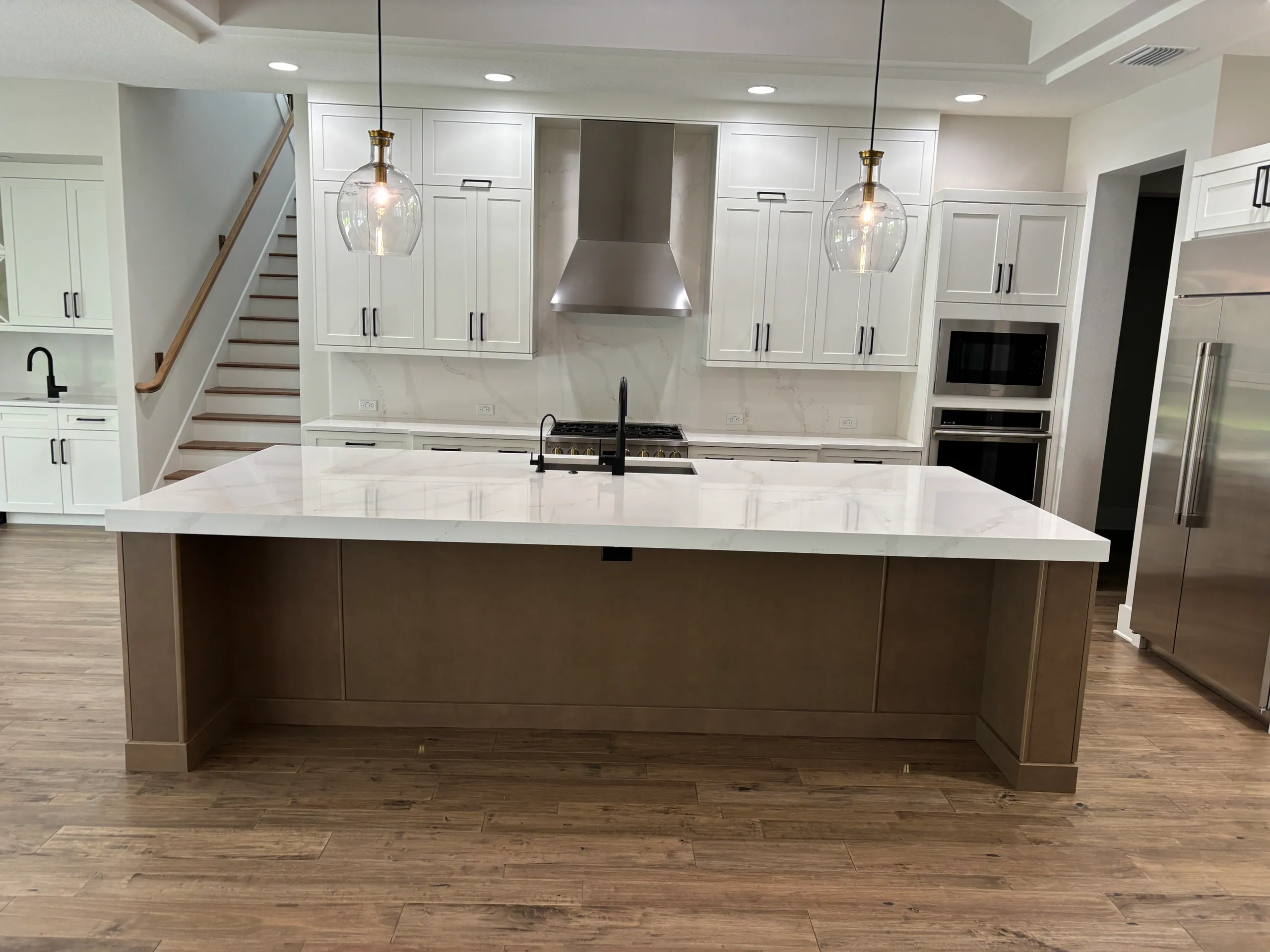 Kitchen inspiration with a broad white island, warm wood base, and pendant lights